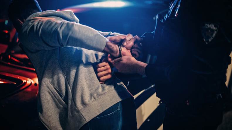 A person in handcuffs is being arrested by an officer. The image highlights the concept of excessive force, a possible legal claim.